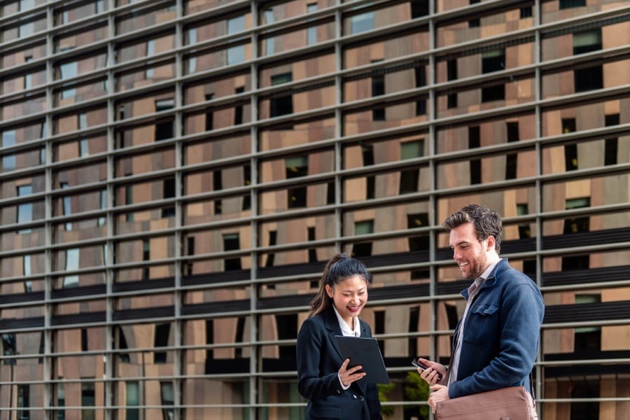 Two colleagues reviewing a tablet outside an office building