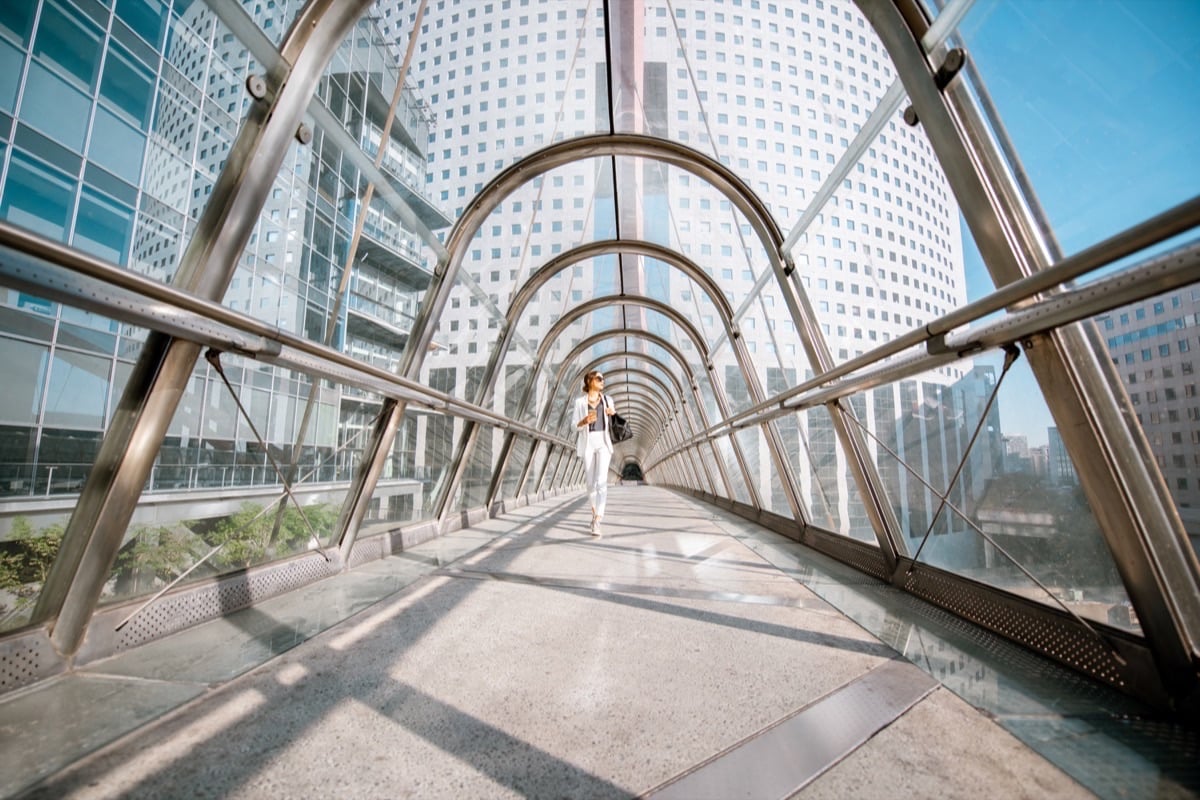 A person walking through a glass-covered bridge between office buildings